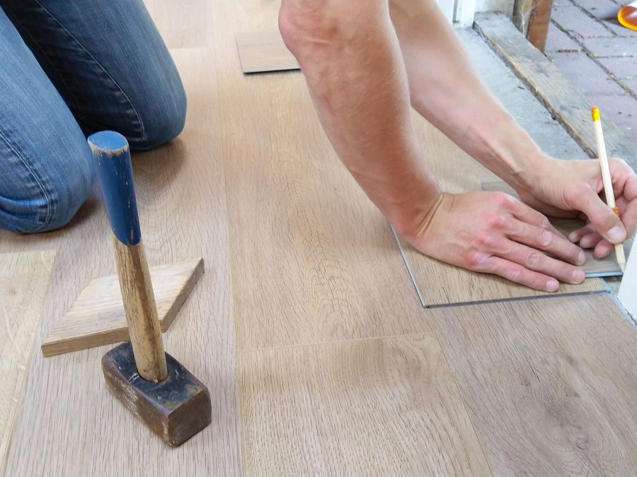 Handwerker misst und verlegt Parkettdielen mit Hammer und Schlagholz