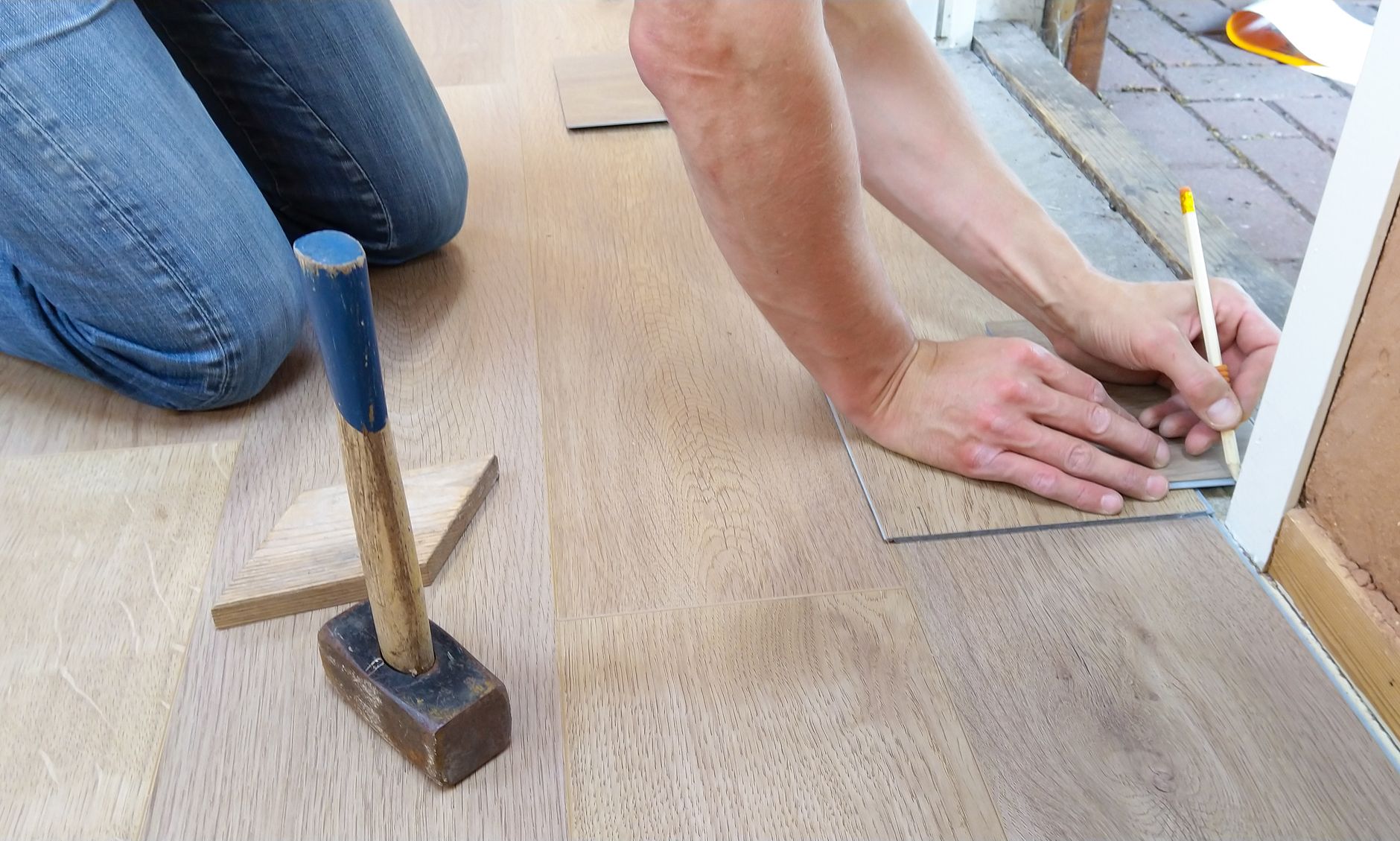 Handwerker misst und verlegt Parkettdielen mit Hammer und Schlagholz